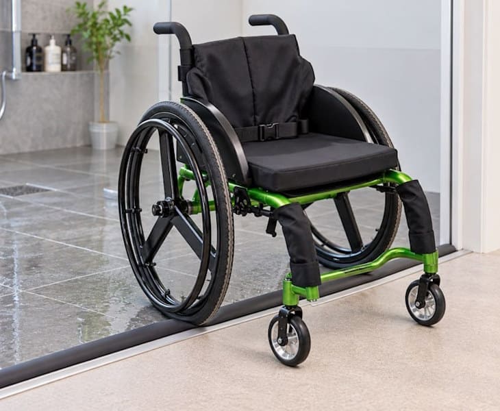 Wheelchair crossing a compressible wet room threshold between wet and dry flooring